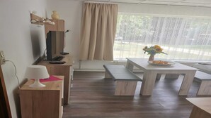 A modern room with a wooden desk, a television, a bench, and a table with a vase of flowers. - Lakeside Escape With Garden Fun (Goldberg)
