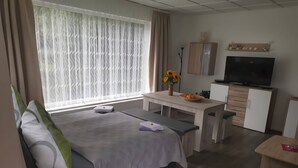 A hotel room with a bed, a desk, a TV, and a window with curtains. - Lakeside Escape With Garden Fun (Goldberg)