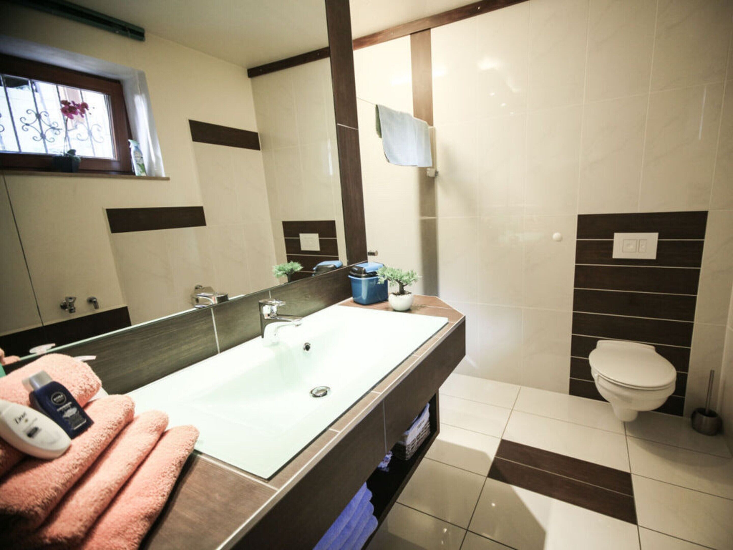 A modern bathroom with a large mirror, a white sink, a toilet, and a shower area.