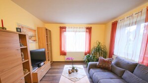 Een woonkamer met een houten kast, een televisie, een bank, een salontafel en een raam met gordijnen.