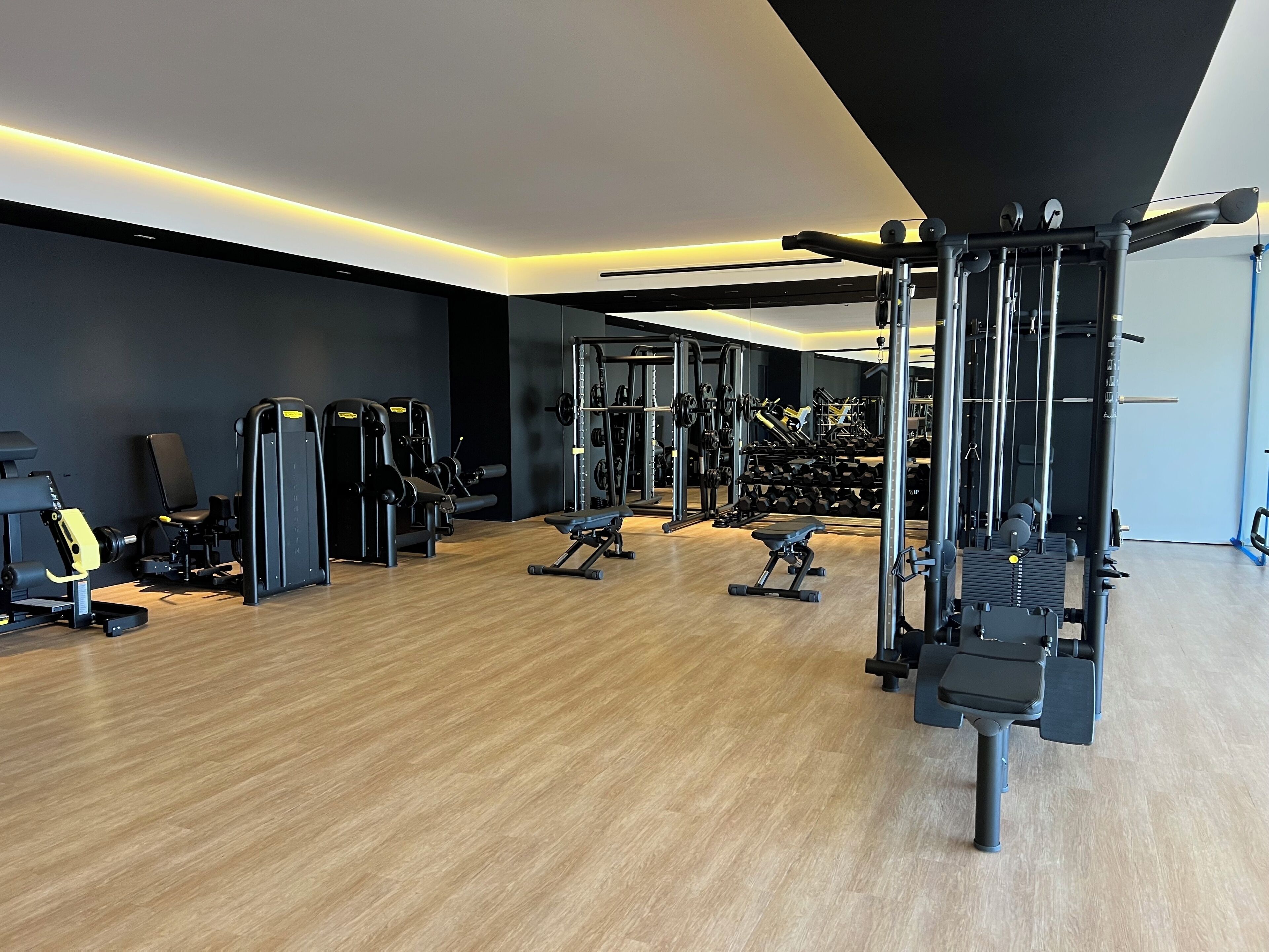 A modern gym with various weightlifting equipment, benches, and a mirrored wall.