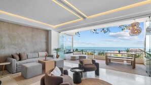 Un salon moderne avec un canapé, des fauteuils et une table basse. Il y a un balcon avec vue sur la mer.