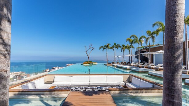 Une piscine d’hôtel avec une terrasse en bois, des chaises longues et des palmiers.