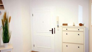 A room with a white door, a white dresser with drawers, a small white table with a plant, and a wooden floor. - Comfy Apartment With 1 Bedroom and Balcony 134 (Binz)