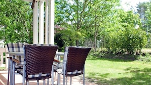 An outdoor patio with wicker chairs and a table, surrounded by a garden and trees. - Comfy Apartment With 1 Bedroom and Balcony 134 (Binz)