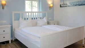 A bedroom with a white bed, two bedside tables, a window, and a painting on the wall. - Comfy Apartment With 1 Bedroom and Balcony 134 (Binz)