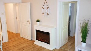 A room with a fireplace, wooden flooring, white walls, and a door leading to another room. - Comfy Apartment With 1 Bedroom and Balcony 134 (Binz)