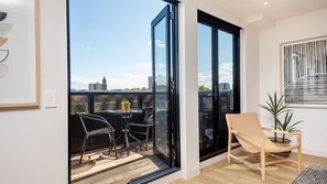 Enjoy the city view from this spacious balcony with a glass door leading to a seating area with two chairs and a table.