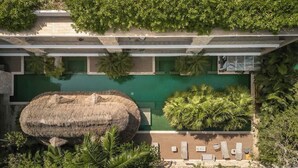 A modern building with a rooftop pool, surrounded by lush greenery and a large thatched structure. - Jungle Jade Penthouse Private Rooftop Pool Oasis (Tulum)