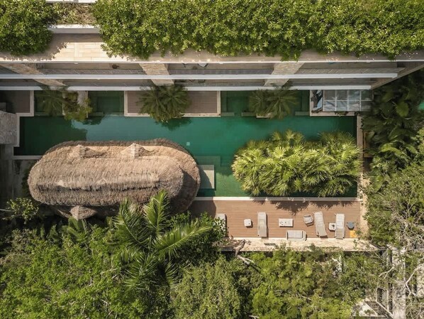 A modern building with a rooftop pool, surrounded by lush greenery and a large thatched structure. - Jungle Jade Penthouse Private Rooftop Pool Oasis (Tulum)
