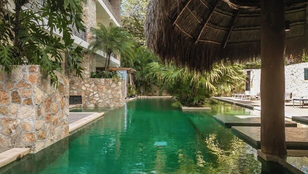 A swimming pool with stone walls, a thatched roof structure, and lush greenery. - Jungle Jade Penthouse Private Rooftop Pool Oasis (Tulum)