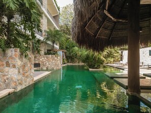 A swimming pool with stone walls, a thatched roof structure, and lush greenery. - Jungle Jade Penthouse Private Rooftop Pool Oasis (Tulum)
