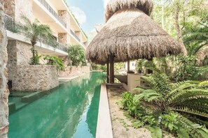 Une piscine dotĂ©e dâune structure avec toit de chaume, de murs en pierre et dâune vĂ©gĂ©tation luxuriante.