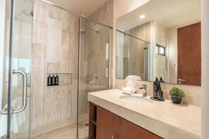Une salle de bain moderne avec une douche Ă parois de verre, un meuble-lavabo avec un miroir et une petite plante en pot.