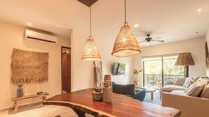 A modern living room with a wooden dining table, hanging wicker lamps, and a sofa. - Jungle Jade Penthouse Private Rooftop Pool Oasis (Tulum)