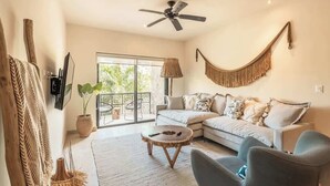 A living room with a sofa, chairs, a coffee table, a ceiling fan, a hammock, and a large window. - Jungle Jade Penthouse Private Rooftop Pool Oasis (Tulum)