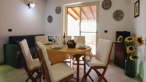 Un comedor con una mesa de madera dispuesta para cuatro personas, rodeada de sillas blancas con cojines. Hay platos decorativos en las paredes y un jarrón con girasoles sobre la mesa.