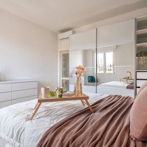 A modern bedroom with a large bed, a bedside table with a tray, a mirror, and a green chair. - Sardinia Re - Emerald House (Sassari)