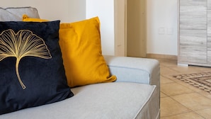 A modern living room with a grey sofa, a yellow and black decorative pillow, and a minimalist wooden cabinet. - Sardinia Re - Emerald House (Sassari)