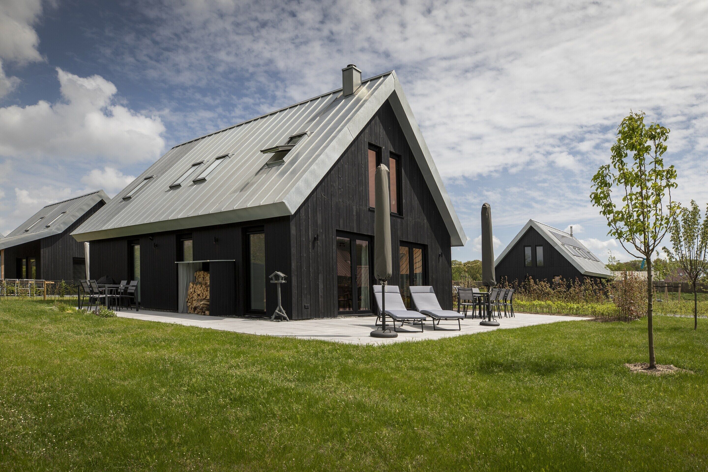 A modern house with a sloped roof, large windows, and a patio with outdoor furniture.