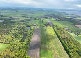 Vista aérea de un paisaje rural con campos, un pequeño pueblo y una masa de agua a lo lejos.