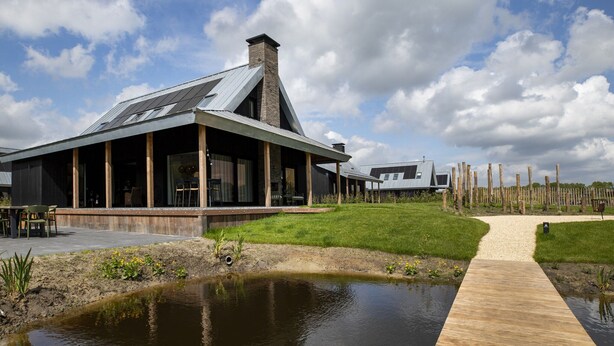 Een modern gebouw met een schuin dak, grote ramen en een houten terras.