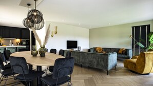 Een moderne woonkamer met een ronde eettafel, zwarte stoelen, een grijze bank en een gele fauteuil.