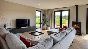 Een moderne woonkamer met een grijze bank, een flatscreen-tv, een klein bijzettafeltje en een open haard.