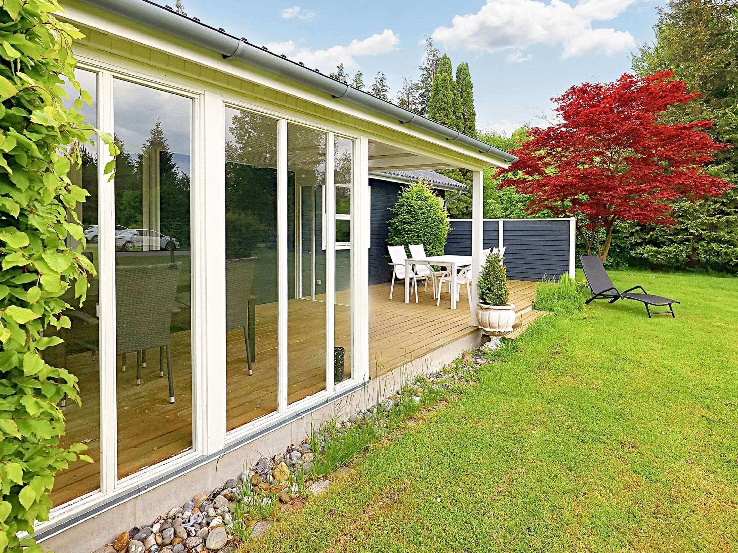 A modern house with a covered patio, a lawn, and a red tree.