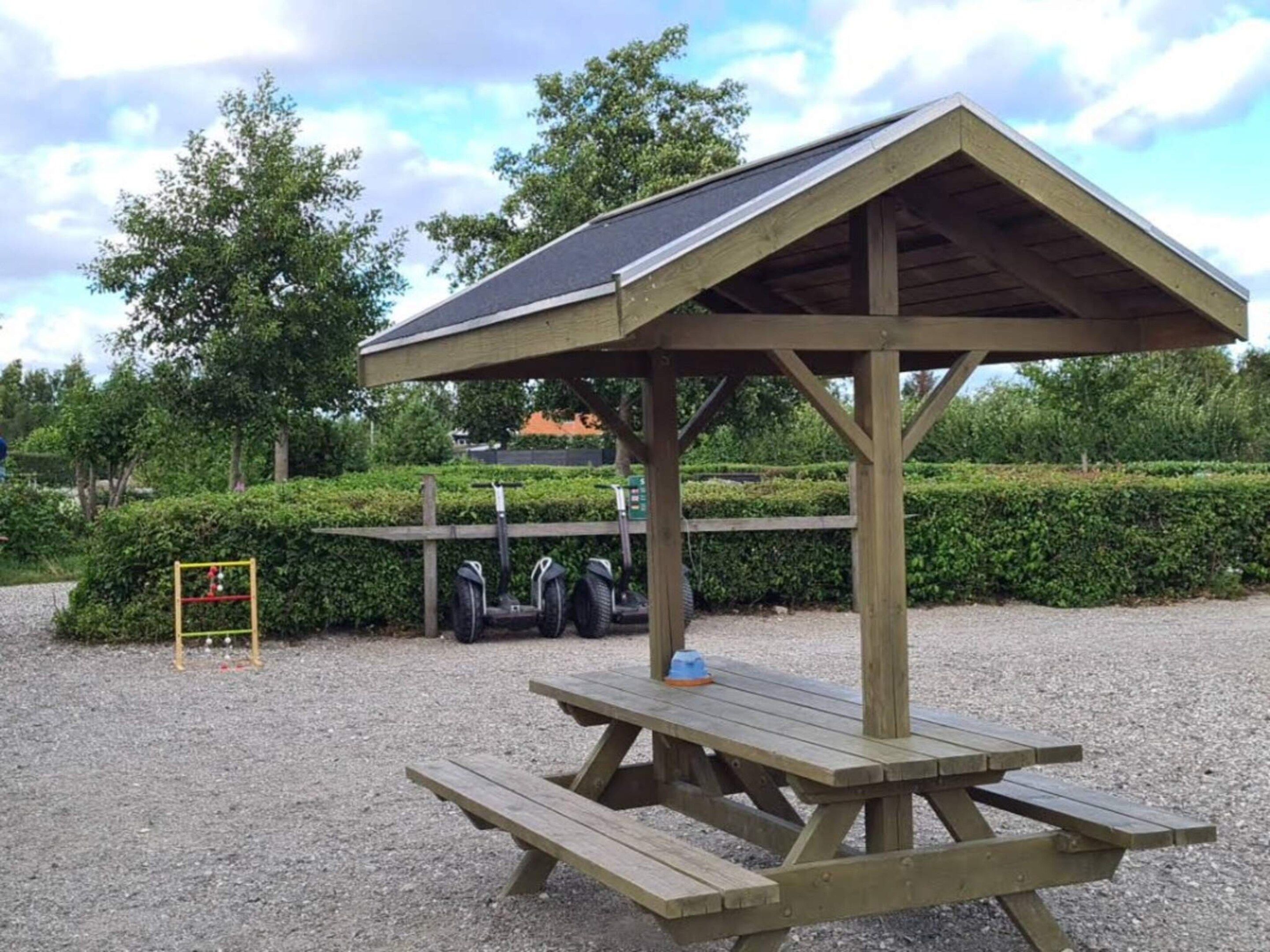 Un refugio de madera para picnic con techo inclinado y una mesa.