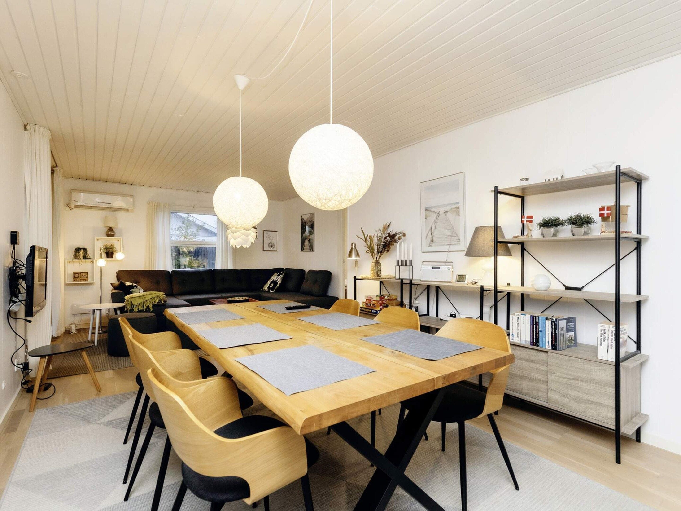A modern living room with a wooden dining table, black and yellow chairs, a black sofa, and a bookshelf with decorative items.
