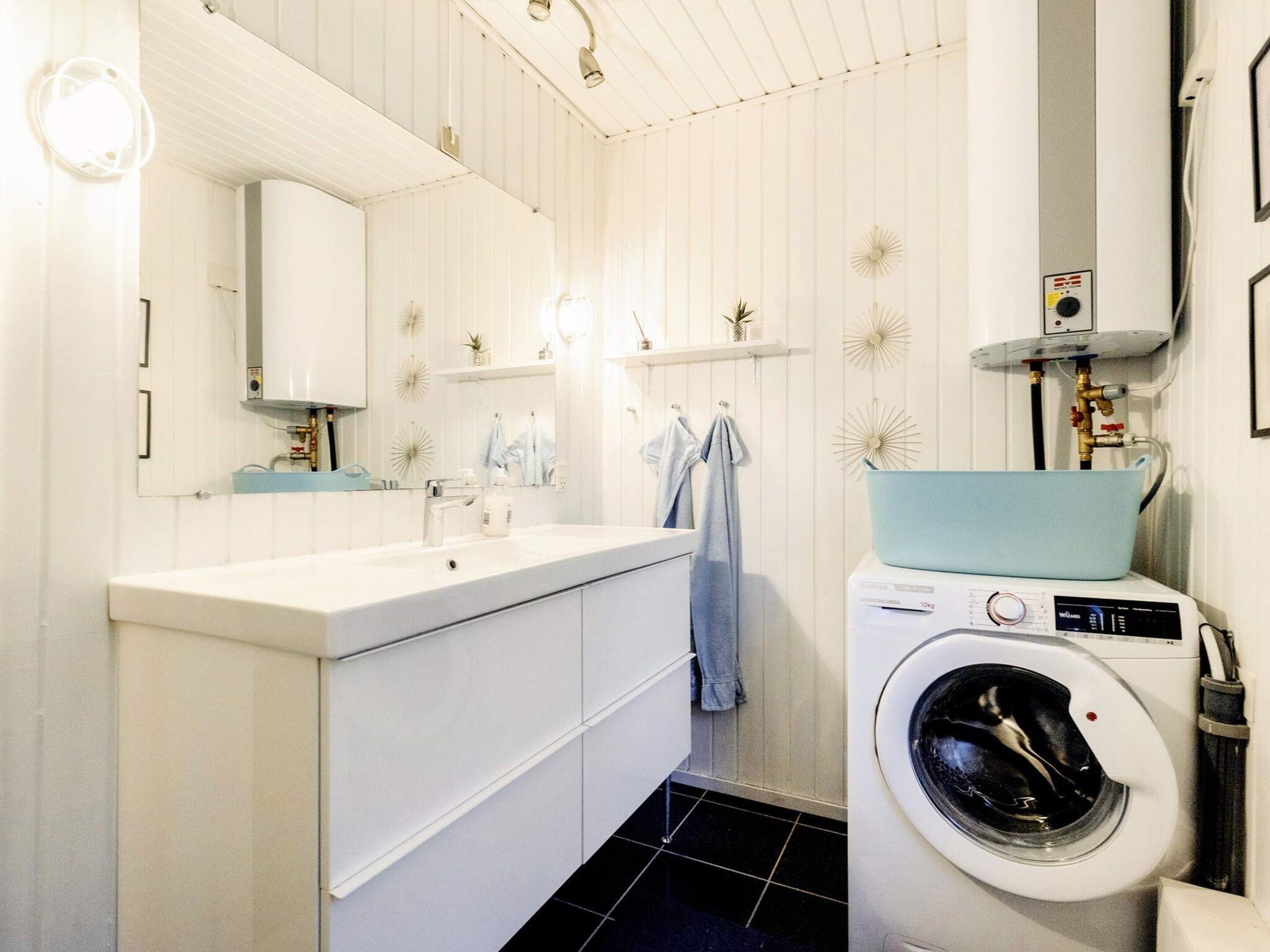 Ein modernes Badezimmer mit einem weißen Waschtisch, einer eingebauten Waschmaschine und einem großen Spiegel.