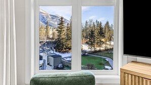 A room with a large window offering a view of a snowy landscape, a green lawn, and a building with a chimney.