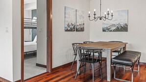 Un comedor con una mesa de madera, sillas negras y un banco. Hay dos cuadros en la pared y una lámpara de araña.