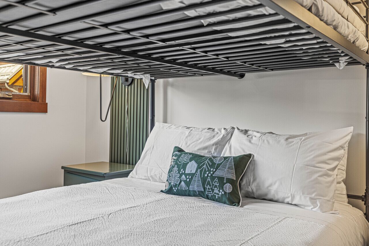 A bunk bed with a white mattress and a green pillow with a geometric pattern.