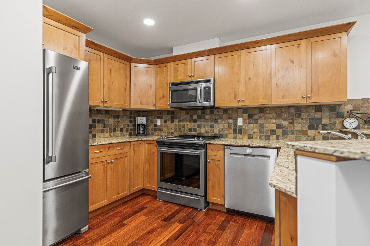 A modern kitchen with wooden cabinets, stainless steel appliances, and a tiled backsplash.