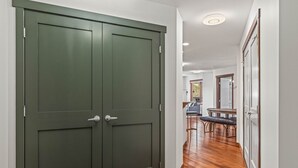 Un pasillo con un par de puertas, suelo de madera y un comedor al fondo.