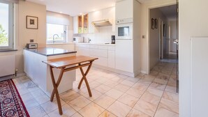 A modern kitchen with white cabinets, a wooden table, and a window. - Apartment Near Koksijde by the Sea (Koksijde)