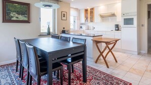 A modern kitchen with white cabinets, a microwave, and a coffee maker. There is a dining area with a table and chairs, and a rug on the floor. - Apartment Near Koksijde by the Sea (Koksijde)