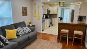 A living room with a sofa, a coffee table, and a kitchen area with a bar and stools. - SUMMER FUN IN A 3BED/2BATH SINGLE FAMILY HOME! (Belmar)