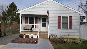 A single-story house with a front porch, a small garden, and an American flag. - SUMMER FUN IN A 3BED/2BATH SINGLE FAMILY HOME! (Belmar)