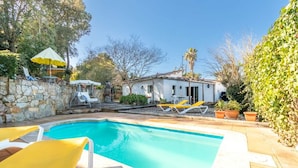 Une piscine rectangulaire avec un mur en pierre d’un côté et un bâtiment blanc en arrière-plan.