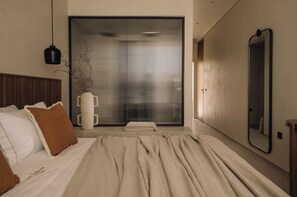 Une chambre moderne avec un grand lit, une table de chevet, un miroir et une vue sur l’extérieur, accessible par une porte coulissante.