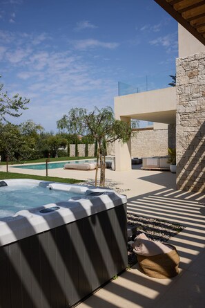 A hot tub in a sunny outdoor setting with a pool and stone walls.
