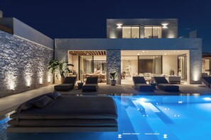 Un espace piscine extérieur moderne, doté de chaises longues et d’un coin repas.