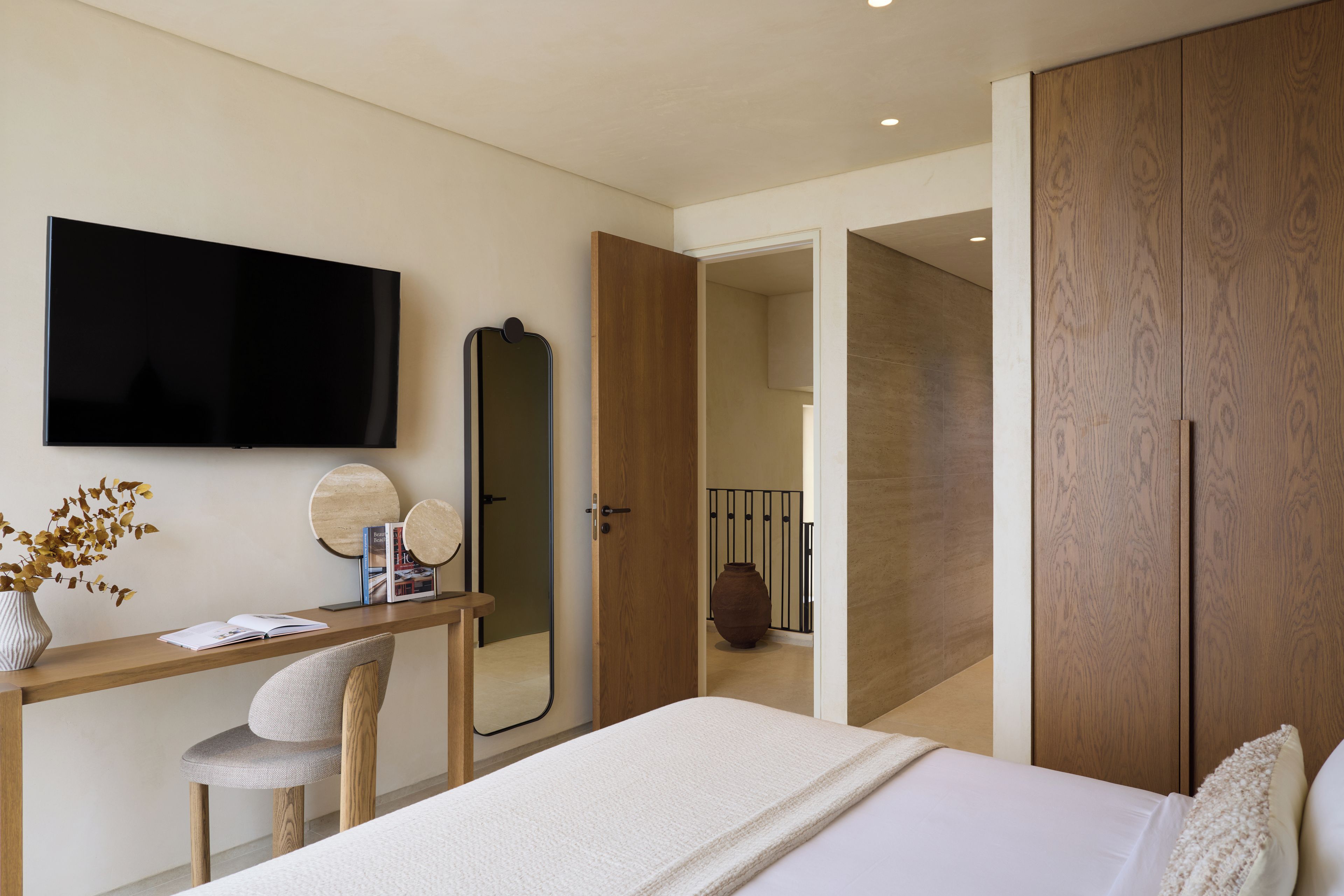 A modern bedroom with a bed, a desk, a chair, a television, a mirror, and a wardrobe.