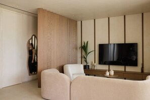 Un salon moderne avec un téléviseur à écran plat fixé au mur, un grand miroir et deux canapés de couleur beige.