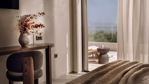 Una habitación moderna con vista al mar, un escritorio con un florero de flores secas y una zona de cama acogedora.