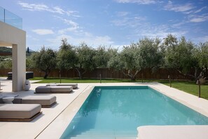 A modern outdoor pool area with lounge chairs and a wooden fence in the background.