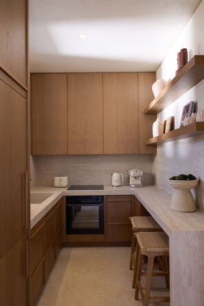 Une cuisine moderne avec des meubles en bois, un four encastré, une machine à café et une étagère où sont exposés des objets décoratifs.
